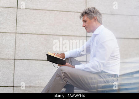 Mature businessman sitting on stairs looking at notebook Stock Photo