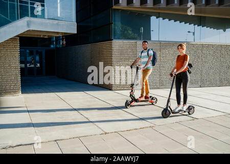 Couple with backpacks riding electric scooters Stock Photo