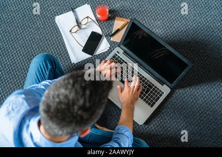 Man sitting on the floor at home using laptop, top view Stock Photo