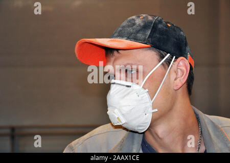 Young man in a dust mask and dusty cap at work. Stock Photo