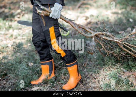 Lumberjack in protective workwear carrying tree branches while logging in the forest, close-up with no face Stock Photo