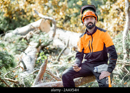 Portrait of a professional lumberman in protective workwear sitting on the felled tree while resting after the hard work in the forest Stock Photo