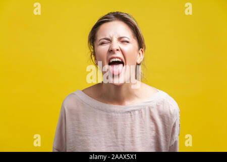 Portrait of young naughty woman with blonde hair in casual beige blouse standing with closed eyes and tongue out, teasing grimace, facial expression. Stock Photo
