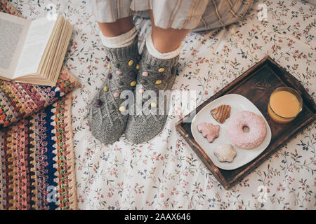 Young woman lying on colorful bed having breakfast on holidays. Morning in a cozy warm bedroom with natural juice Christmas cookies and and donut. Hap Stock Photo