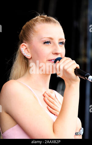 Young blonde blue eyed women, Gallia, performing on stage at the Faversham Hop festival. Close up as she sings into microphone in pink top. Stock Photo
