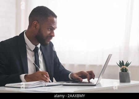 Concentrated business clerk making notes, using laptop Stock Photo