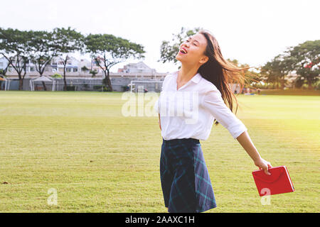Young and pretty girl feeling happy on greenfield. Optimistic smiling asian student release stress after studying Stock Photo