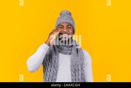 Smiling black guy in knitted winter set talking by phone Stock Photo