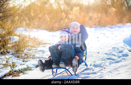 Children play in a snowy winter park at sunset. Sledding down the hill and having fun. Winter fun. Holidays. Stock Photo