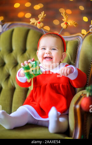 Cute little girl in a red dress is sitting on the sofa and having fun. Christmas and New Year Stock Photo