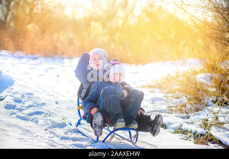 Children play in a snowy winter park at sunset. Sledding down the hill and having fun. Winter fun. Holidays. Stock Photo