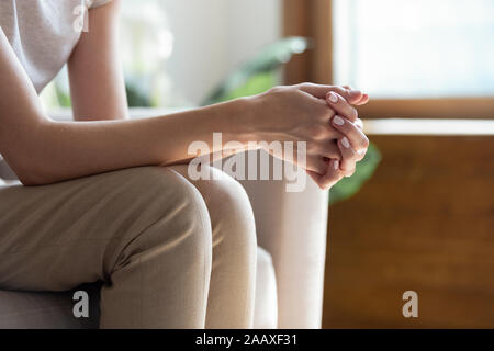 Closeup woman sitting on sofa with folded hands on knees. Stock Photo