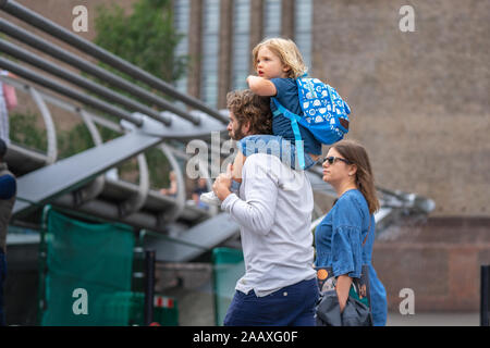 London, UK, July, 2019. Little boy sitting on father's shoulders near Millennium Bridge over the River Thames in London. Stock Photo