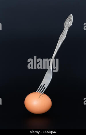 A brown egg pierced with a fork, with cracks in the shell, on a dark blue background Stock Photo
