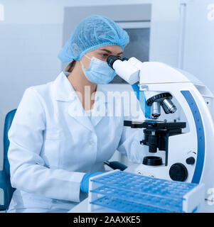Laboratory worker using modern microscope in mask and gloves Stock Photo