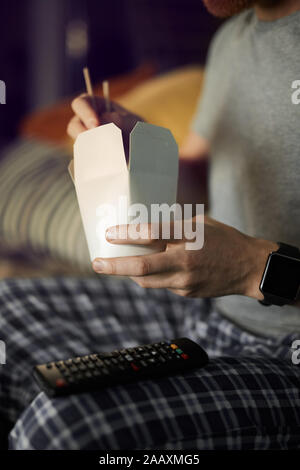 Close up of unrecognizable man watching TV in dark and eating takeout noodle while enjoying late night movies, copy space Stock Photo