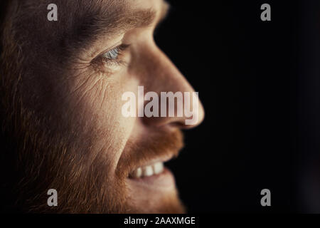 Side view closeup of handsome adult man smiling happil y while watching TV at night, profile outlined against dark background, copy space Stock Photo