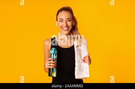 Lady Listening To Music Holding Water And Towel, Yellow Background Stock Photo