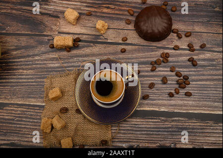 Cup of coffee, the marshmallows in chocalate, brown sugar and coffee beans on wooden background. Close up Stock Photo