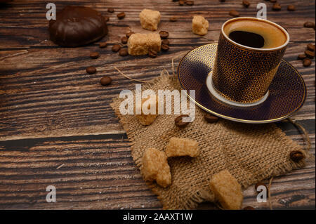 A Cup of coffee, pieces of brown sugar, marshmallows in chocolate and coffee beans on a wooden background. Close up Stock Photo