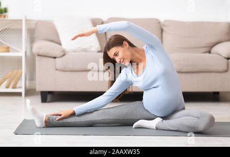 Calm pregnant woman doing stretching exercises at home Stock Photo