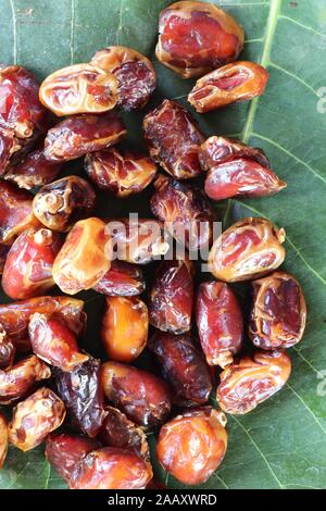 Abstract background of sweet honey dates on the market close up. Delicious fruit - ramadan. Dried organic date fruits on green leaf. Dried dates. Stock Photo