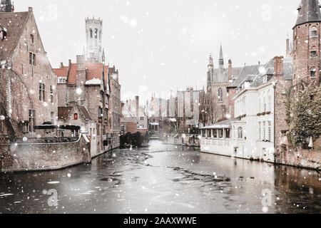 Bruges, Belgium canals view in winter snowfall. Stunning fairy landscape with historical buildings and calm icy water. Christmas mood. Monochromatic n Stock Photo