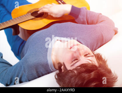 Young man lying back on sofa with guitar Stock Photo