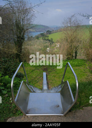 A view from a slide. A children's empty playground slide looking out across the green fields and the river Dart, near Dartmouth, Devon Stock Photo