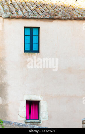 Two colored windows on the stone wall of an old house. Stock Photo