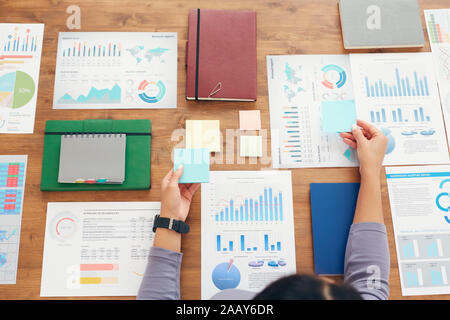 Above view background of unrecognizable businesswoman planning project while working at wooden desk laying out documents and sticker notes, copy space Stock Photo