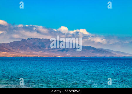 View of the hill on the island Fuerteventura near Morro Jable, Canary islands, Spain. There is clear blue water and beautiful sky. Stock Photo