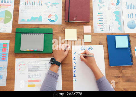 Flat lay background of young woman writing to do list while planning work project sitting at wooden desk, copy space Stock Photo