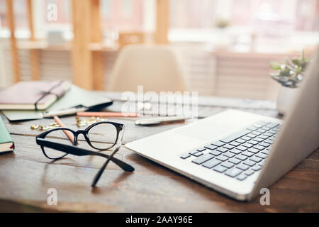Background image of business office with laptop and supplies on wooden desk, focus on black hard rim glasses in foreground, copy space Stock Photo