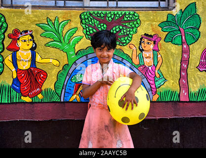 Pingla, West Bengal, India. 23rd Nov, 2019. Village kid plays with a balloon beside a decorated Wall.Naya Village under Pingla Block is a small village under Paschim Midnapore District of West Bengal, India which is famous for their colourful Ancient Folk Art. Almost 60 Families of this village are associated with the Art Patachitra, an ancient folk art of Bengal, the art is appreciated by art lovers all over the world for its style of drawings, shape, pattern, textures and colours. The Art is based on mythological tales and tribal rituals to stories based on modern Indian history and cont Stock Photo