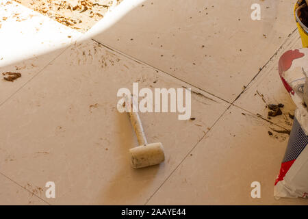 Home renovation of ceramic tiles in an entrance way. Tapping tiles in with rubber mallet a DIY and levelling tiles with mortar and cement. Stock Photo