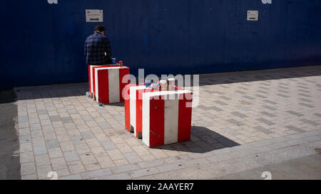 A man sits on concrete safety barriers while taking a break surrounded by waste single use coffee cups discarded by public. Stock Photo