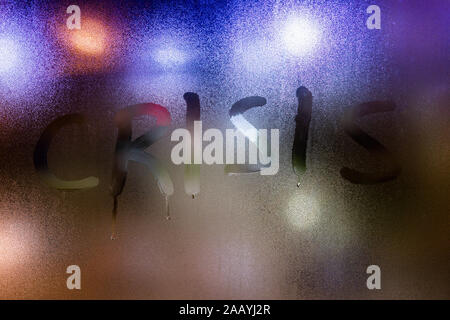 The word crisis written on night wet window glass close-up. Stock Photo