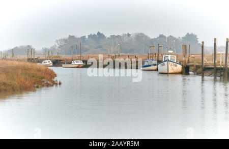 Small traditional fishing boats moored along an inlet at Thornham Old Harbour on the North Norfolk Coast in the hazy evening sun Stock Photo