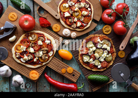 Homemade vegetarian pizza party. Flat lay of gluten free cauliflower and dough pizzas with eggplants, mushrooms, tomatoes and goat cheese decorated wi Stock Photo
