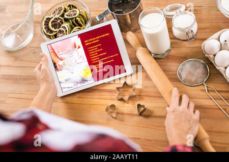 Flat layout of hands of housewife holding touchpad with recipe and rolling-pin before making cookies at home Stock Photo
