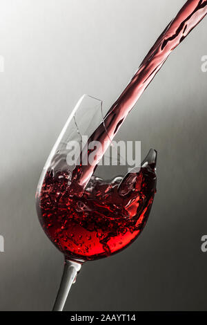 Studio closeup of filling red wine in a a broken wine glass in front of textured background with soft light-dark gradient. Stock Photo