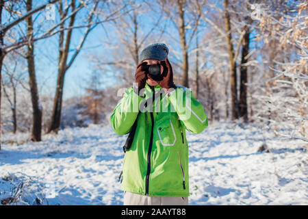 Young photographer takes pictures of winter forest using camera. Young man shooting photos outdoors Stock Photo