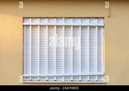 White metal shutters on the window of the facade of the house are closed with a white metal grill. Stock Photo