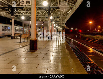 Rainy night at York railway station.  A platform is illuminated by lamps with the light reflected in the wet surface. A 19th Century canopy is above. Stock Photo