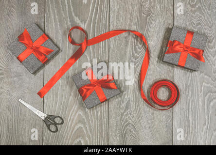 Gift wrapping. Three wrapped presents, in glitter boxes with red ribbon bow, also in photograph are a pair of scissors and a roll of ribbon Stock Photo