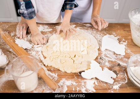 Hands of mother and son in white aprons cutting figures in rolled dough while making tasty cookies for holiday Stock Photo