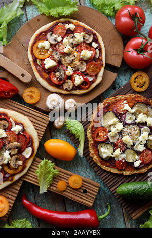 Healthy vegetarian festive food. Homemade thin pizzas with champignons, bell peppers, eggplants and goat cheese with raw ingredients on oak boards on Stock Photo