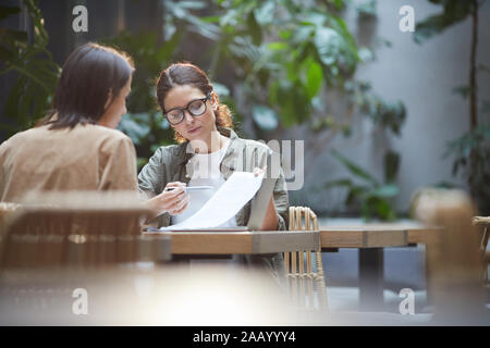 Portrait of two female entrepreneurs discussing project while working at table in outdoor cafe terrace, copy space Stock Photo