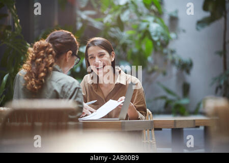 Portrait of cheerful young woman talking to friend or colleague during business meeting on outdoor cafe terrace, copy space Stock Photo